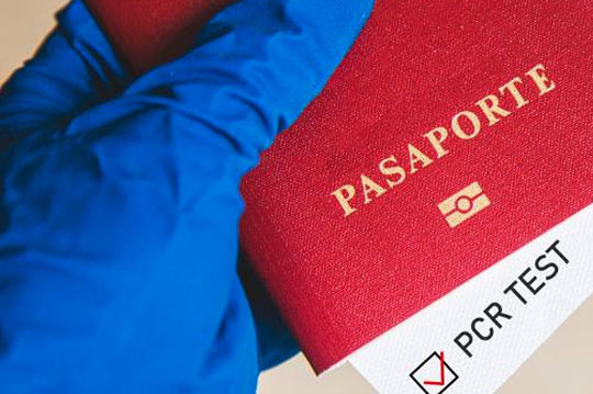 Persona sosteniendo pasaporte con guantes y resultado de test PCR confirmado